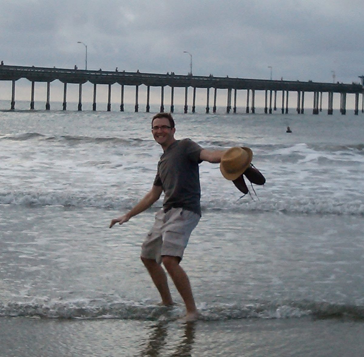 Dave Petry walking in the surf at Ocean Beach pier, San Diego, holding a hat